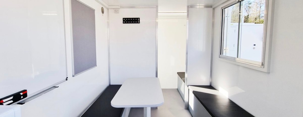 Office area inside the BOXD 16ft welfare unit with bench seating and notice boards